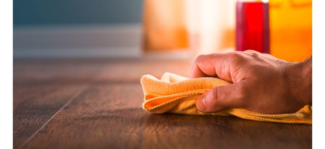 Hand veegt met een oranje doek over een houten vloer